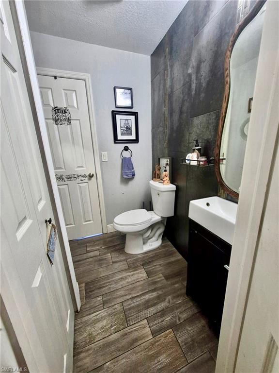 Bathroom featuring wood-look plank tile flooring, a white toilet, and a wall-mounted sink vanity with a dark wood-finish cabinet