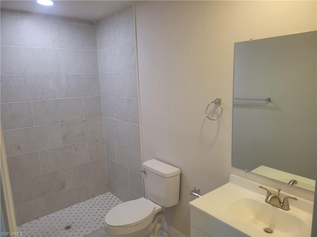 Bathroom featuring a tile shower, vanity, and toilet