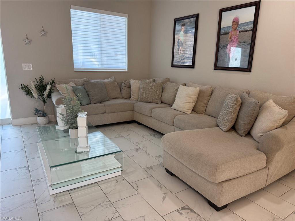 Spacious living area featuring light-toned walls and large format tile flooring