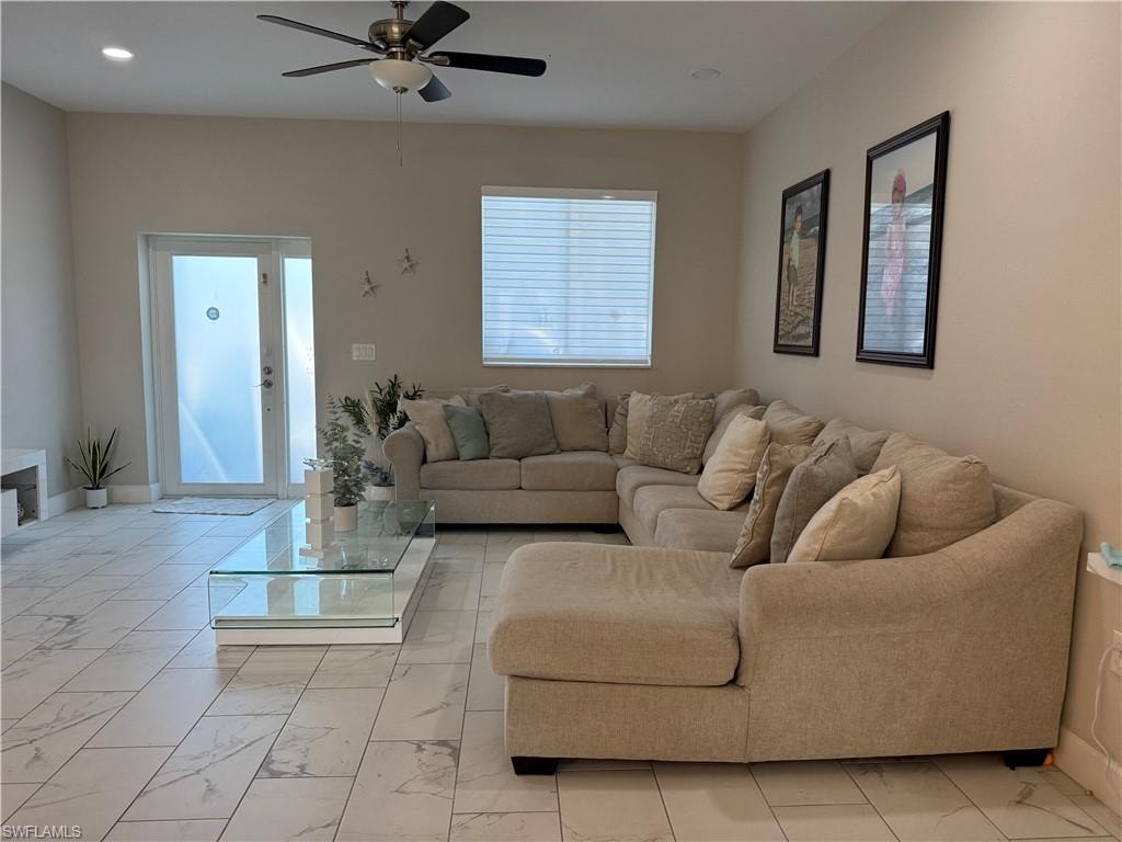Spacious living area featuring large format tile flooring, a frosted glass entry door with sidelight, and a ceiling fan with integrated lighting