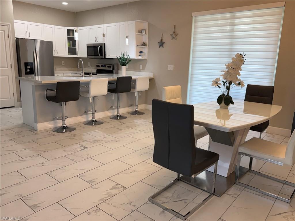 Open-concept kitchen and dining area featuring a kitchen island with seating, stainless steel appliances, white cabinetry, and large format tiled flooring