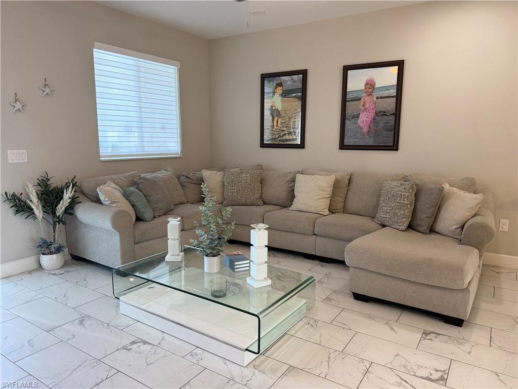 Spacious room featuring light-toned walls, a large window with horizontal blinds, and tile flooring with a subtle veined pattern