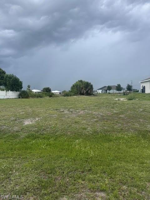 Expansive parcel featuring a large, undeveloped grassy area, perimeter fencing, mature foliage, and residential structures in the distance