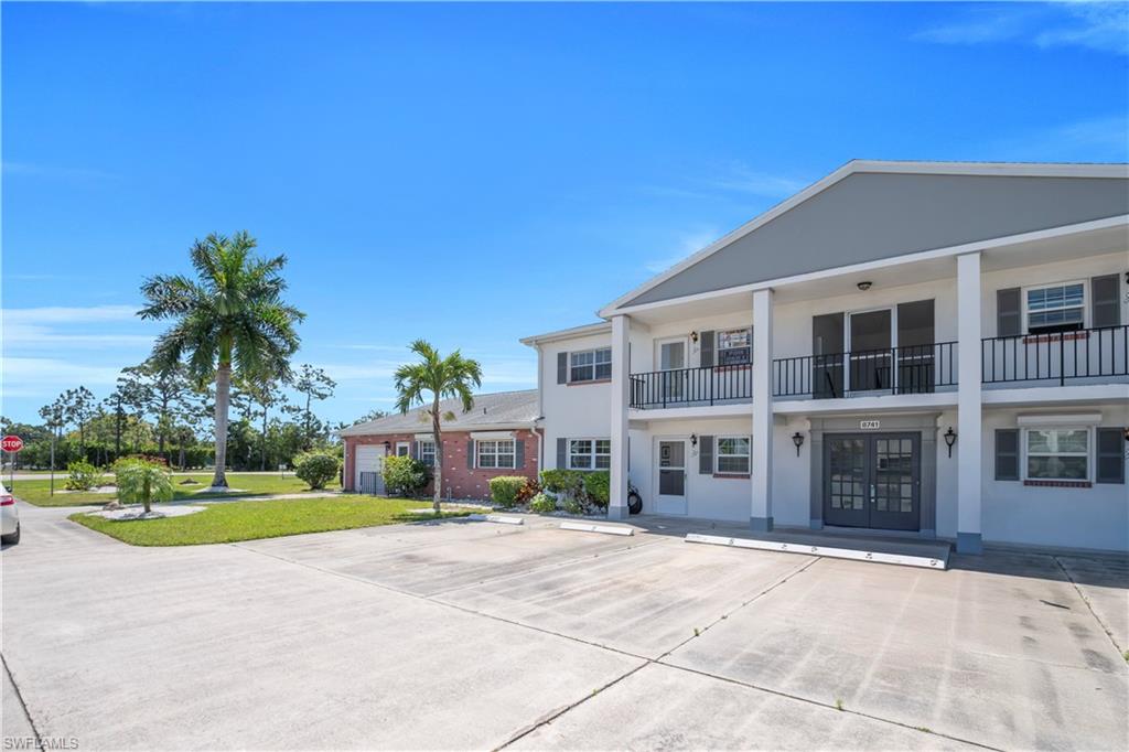 Two-story exterior with a covered balcony, individual unit entrances, and a concrete parking area
