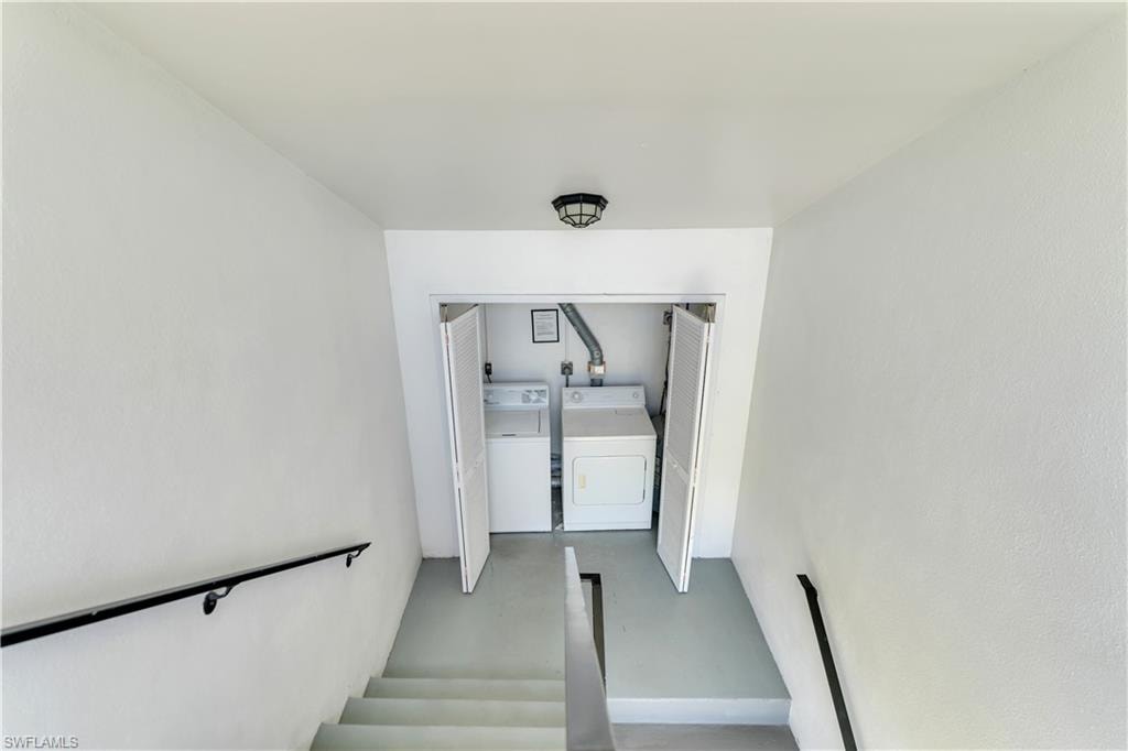 Recessed laundry area with bi-fold doors, featuring a washer and dryer unit, positioned at the base of a staircase with black metal handrails