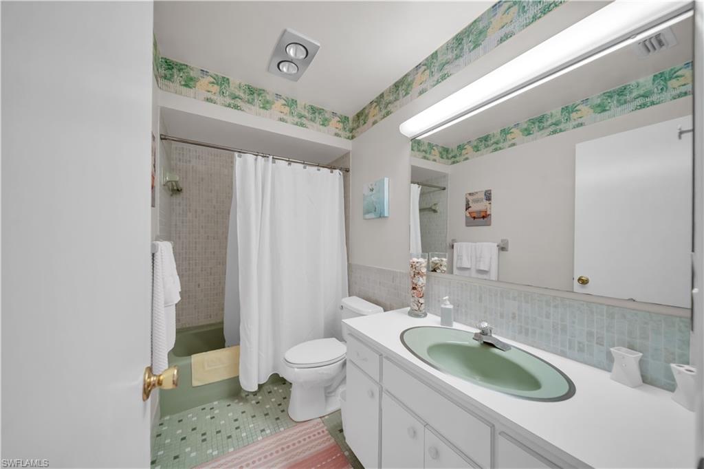 Bathroom featuring a green tub, patterned floor tiles, a vanity with a green sink, and a large wall-mounted mirror