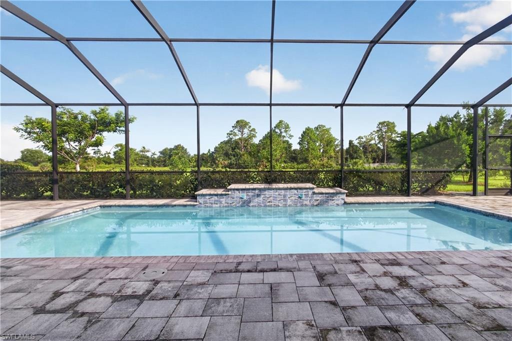 Screened pool enclosure featuring a rectangular pool, integrated spa with mosaic tile, and paver decking