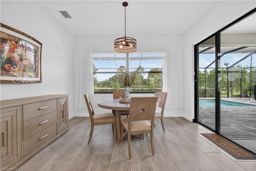 Dining area with wood-finish tile flooring, a contemporary chandelier, and sliding glass doors opening to a screened-in pool patio with pavers