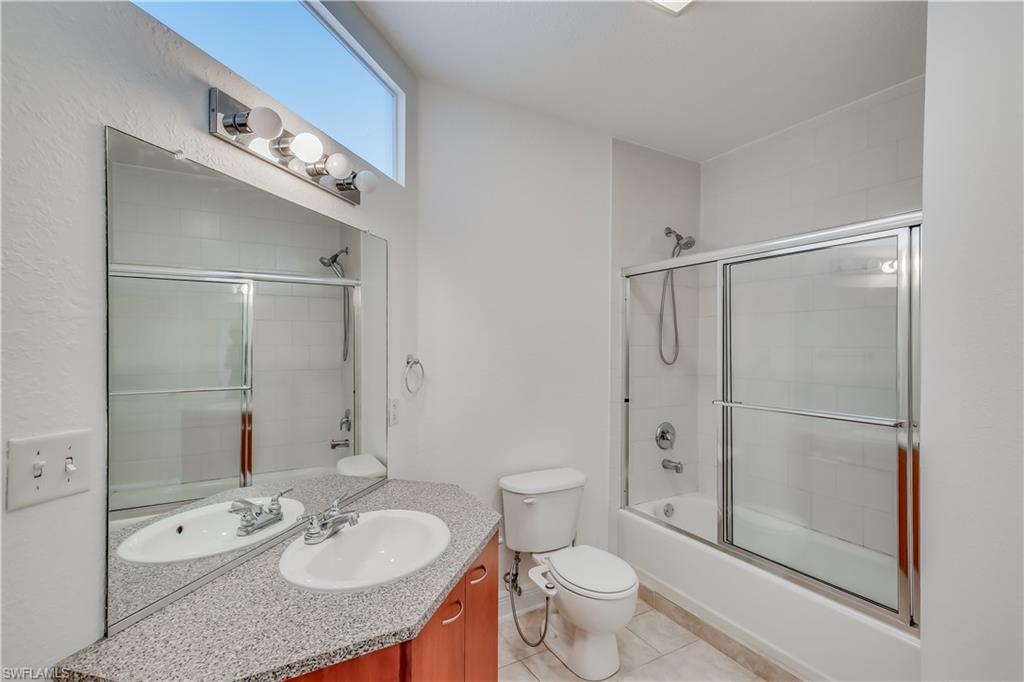 Full bathroom featuring combined bath / shower with glass door, oversized vanity, toilet, and tile floors