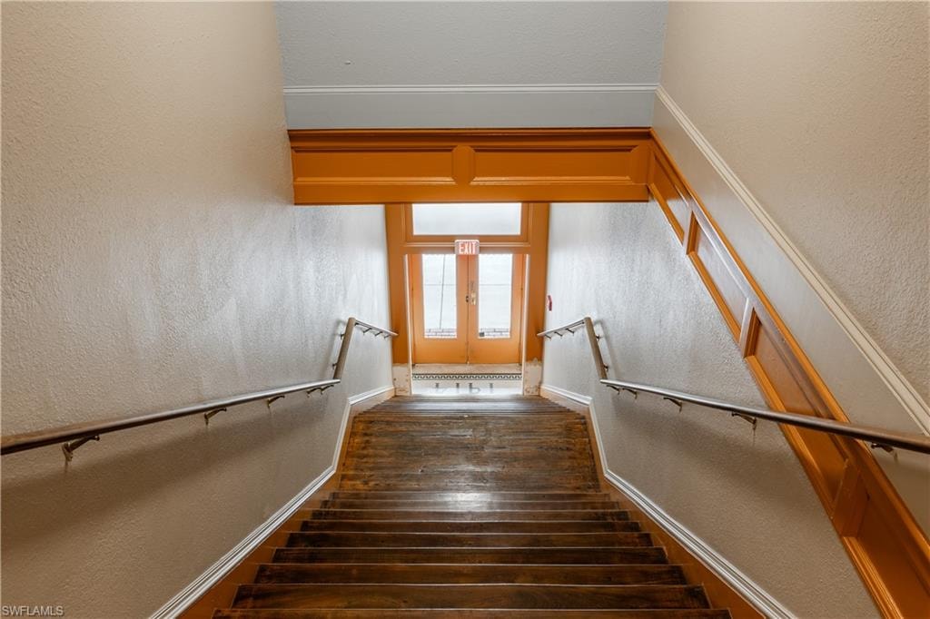 Stairway with french doors, dark hardwood / wood-style floors, and ornamental molding