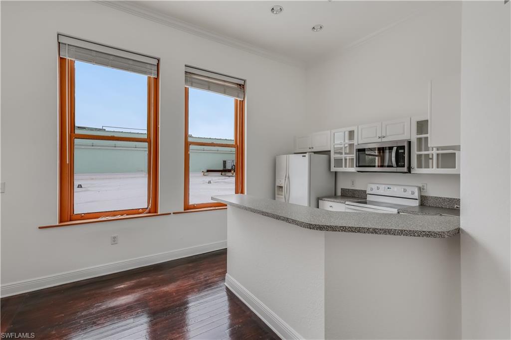Kitchen with dark hardwood / wood-style floors, kitchen peninsula, crown molding, white cabinets, and white appliances