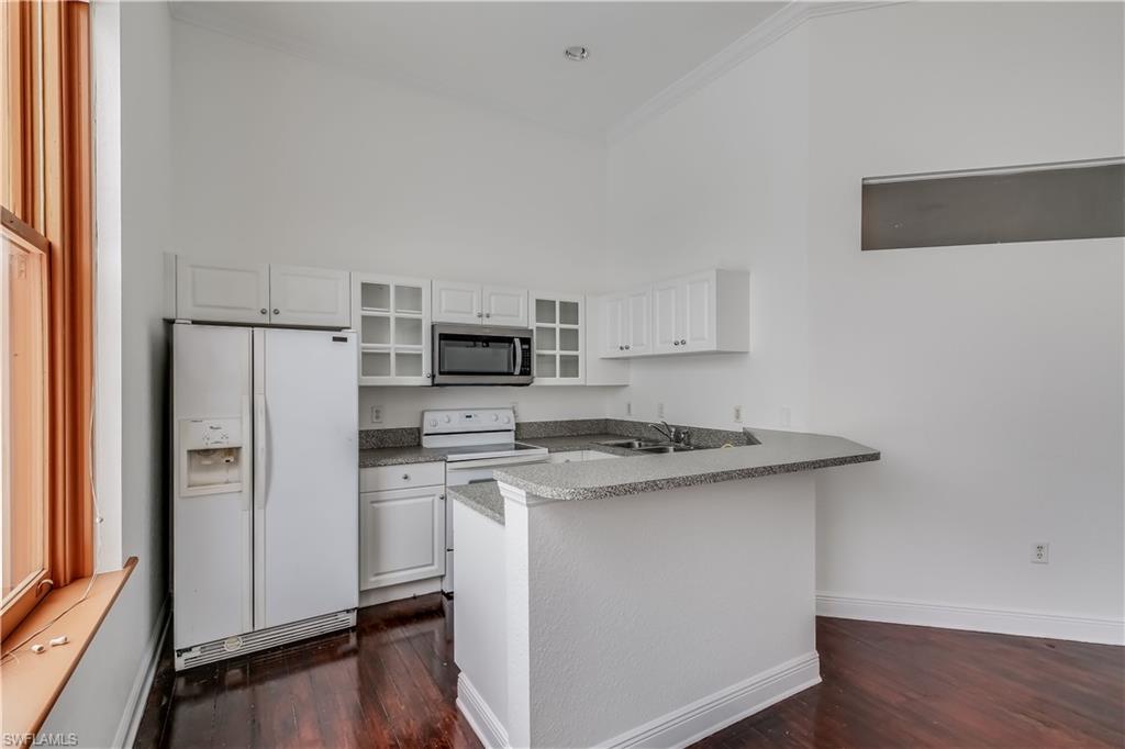 Kitchen with white appliances, dark hardwood / wood-style floors, and white cabinetry