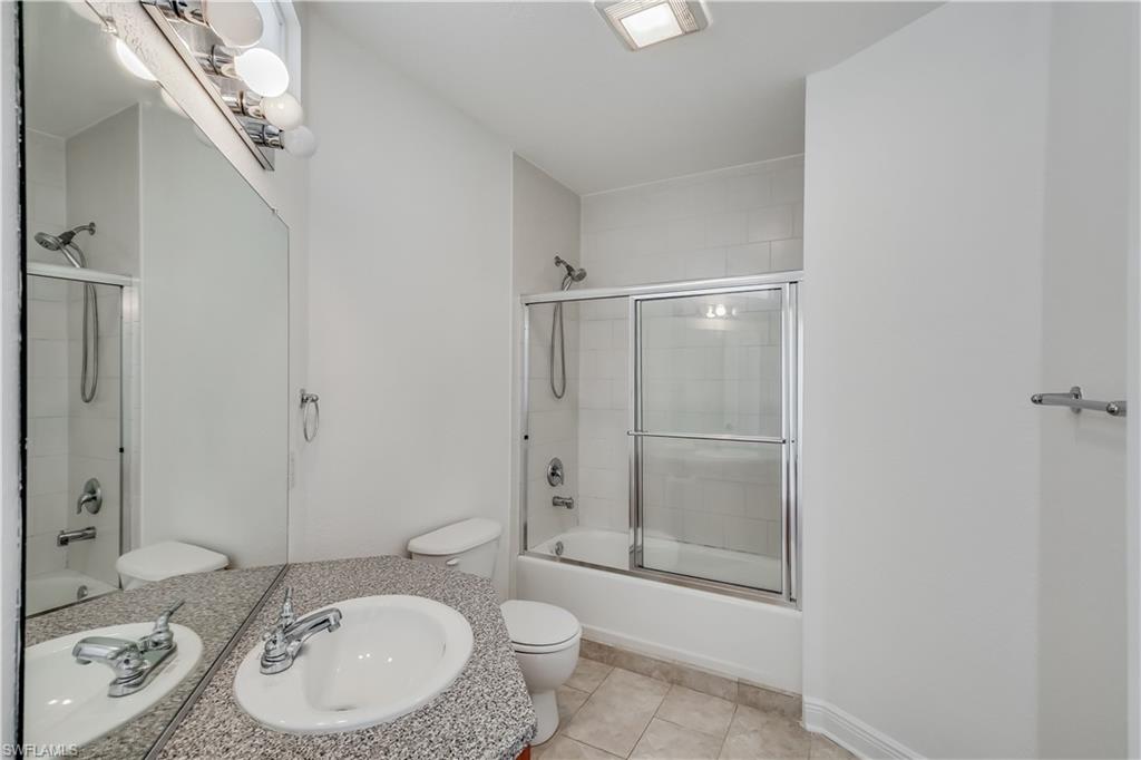 Full bathroom with tile floors, bath / shower combo with glass door, large vanity, and toilet