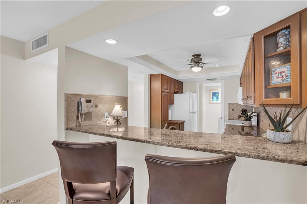 Kitchen featuring a breakfast bar with stone countertop, recessed lighting, ceiling fan, and wood cabinetry with glass-front accents