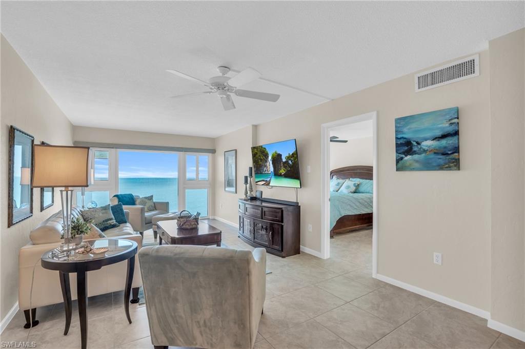 Living area featuring expansive windows, water scenery, tile flooring, a ceiling fan, and an open doorway to an additional room