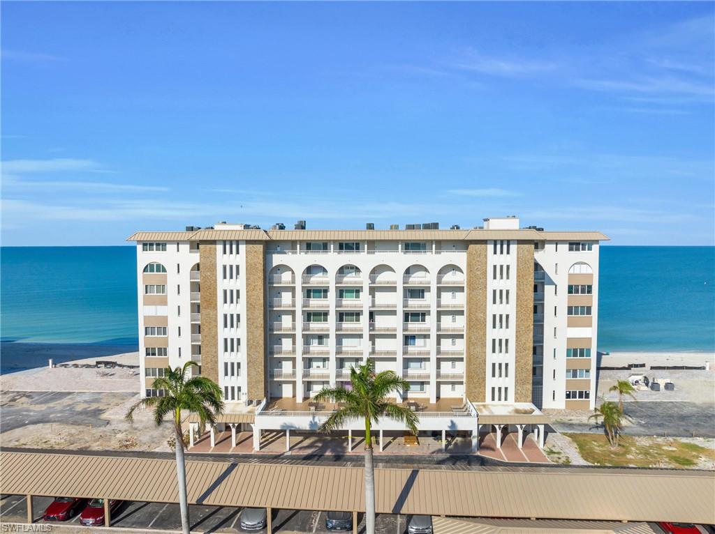 Multi-story condominium building featuring white and tan exterior finishes, arched windows, and private balconies