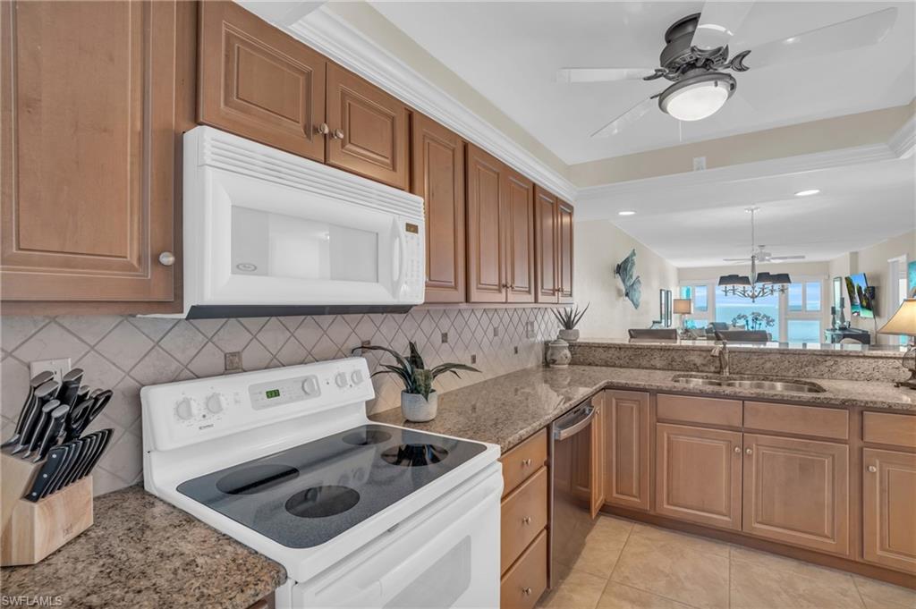 Kitchen featuring light wood cabinetry, granite countertops, a tiled backsplash, and an over-the-range microwave
