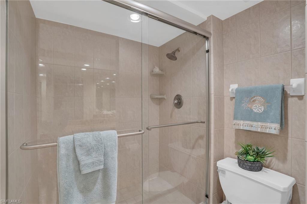 Enclosed shower with clear glass door and brushed nickel hardware, featuring neutral-toned tile walls and a built-in shower niche