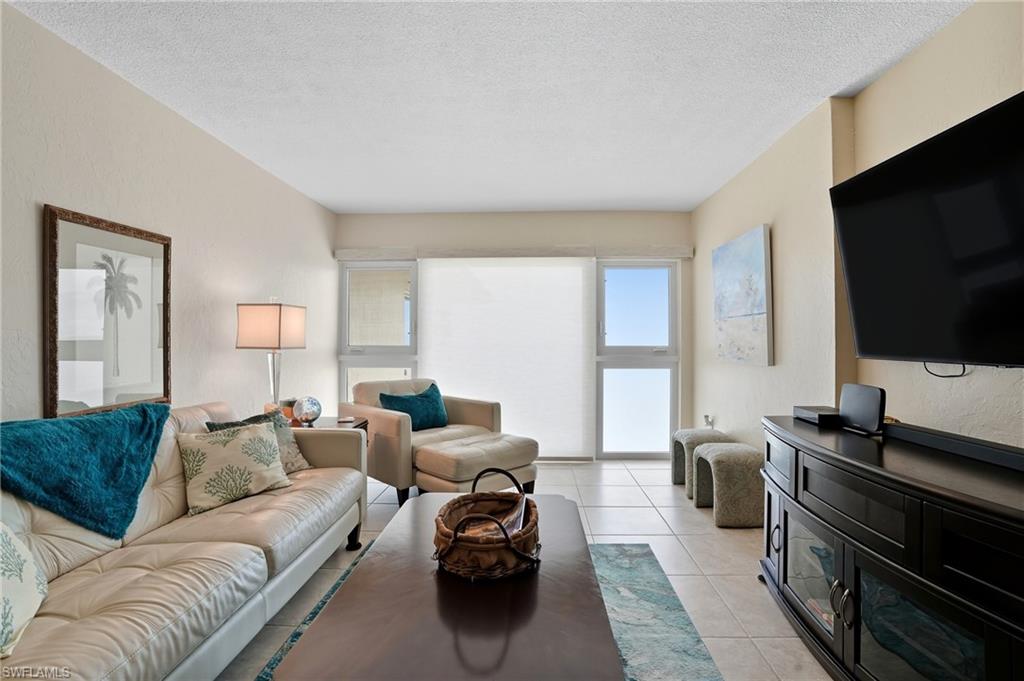 Living area featuring light-toned walls, tile flooring, and large windows with roller shades