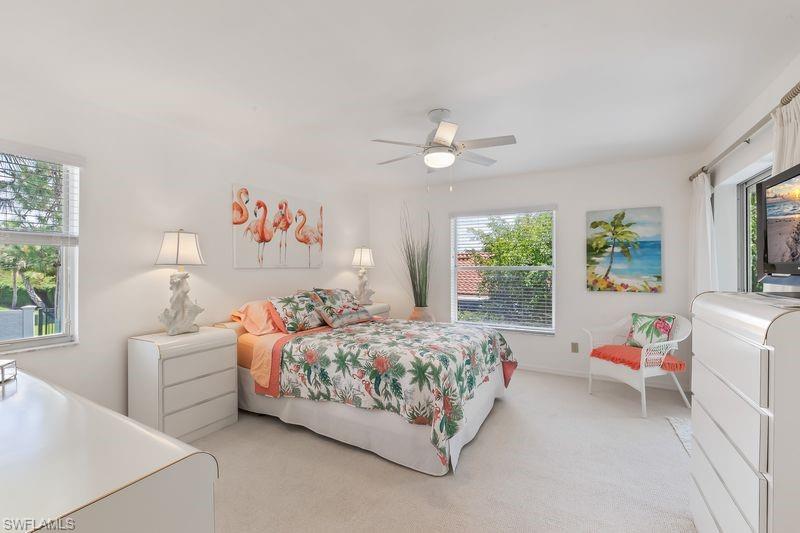 Primary bedroom featuring multiple windows, a ceiling fan with integrated lighting, neutral carpeting, ensuite bath, and slider door out to the screened lanai.