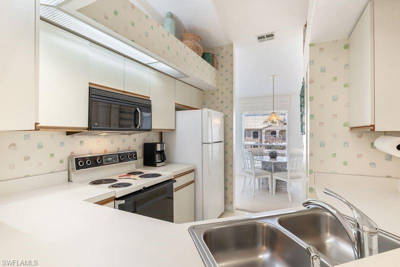 White kitchen featuring white cabinetry and countertops, a double basin stainless steel sink.