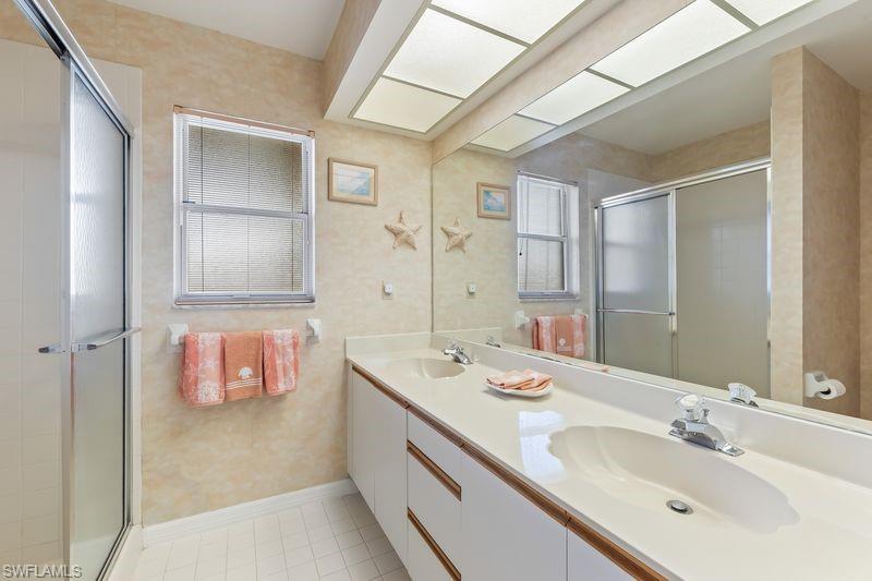 Bathroom featuring a dual-sink vanity with white cabinetry, a large mirrored wall, and walk-in shower.