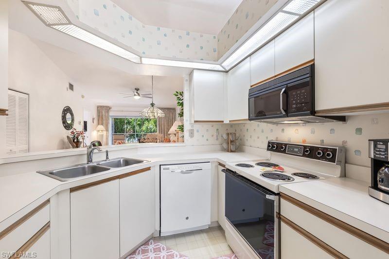 Kitchen featuring white cabinetry with wood-finish trim, a double basin stainless steel sink, and white countertops.