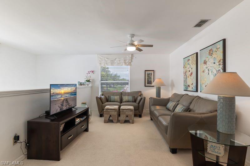 Carpeted living area featuring a new ceiling fan, window with blinds, and white walls.