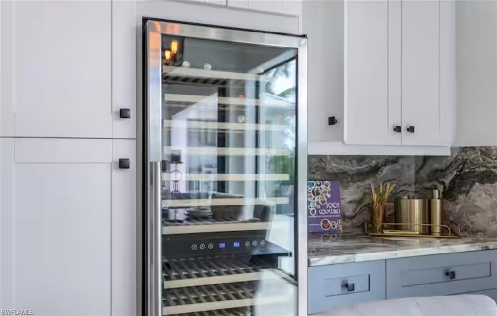 Bar area with wine cooler, decorative backsplash, light stone counters, and dual tone cabinets