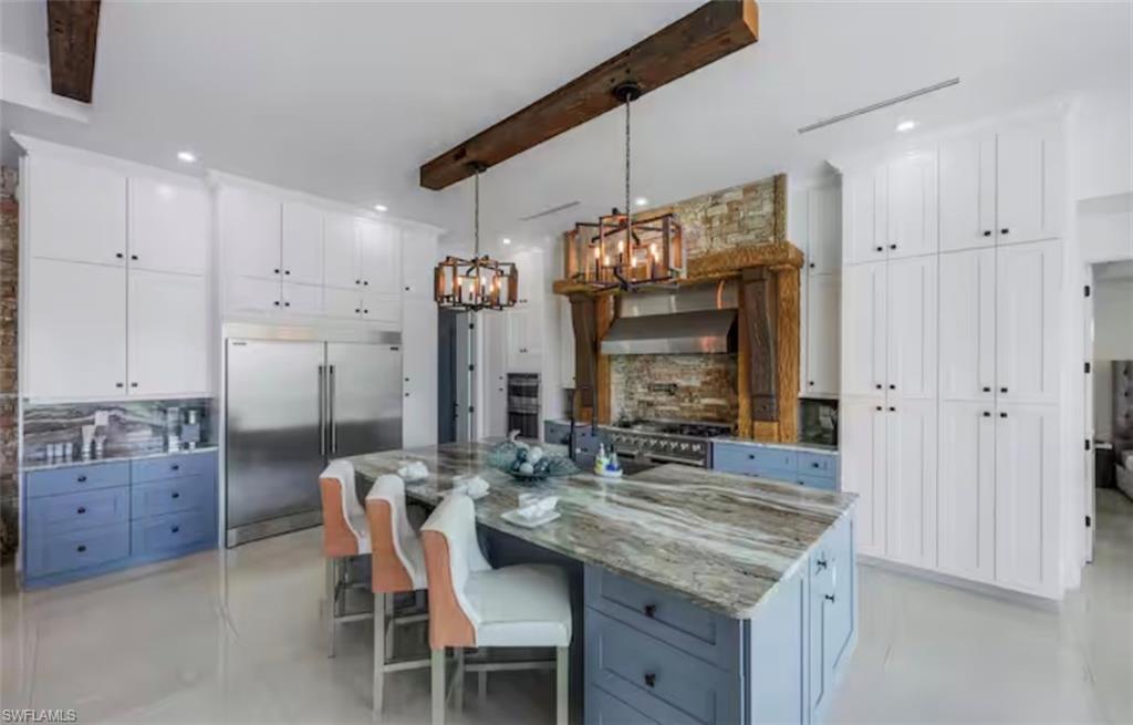 Dual tone kitchen featuring dual tone cabinets, decorative backsplash, beam ceiling, high end appliances, and light stone counters