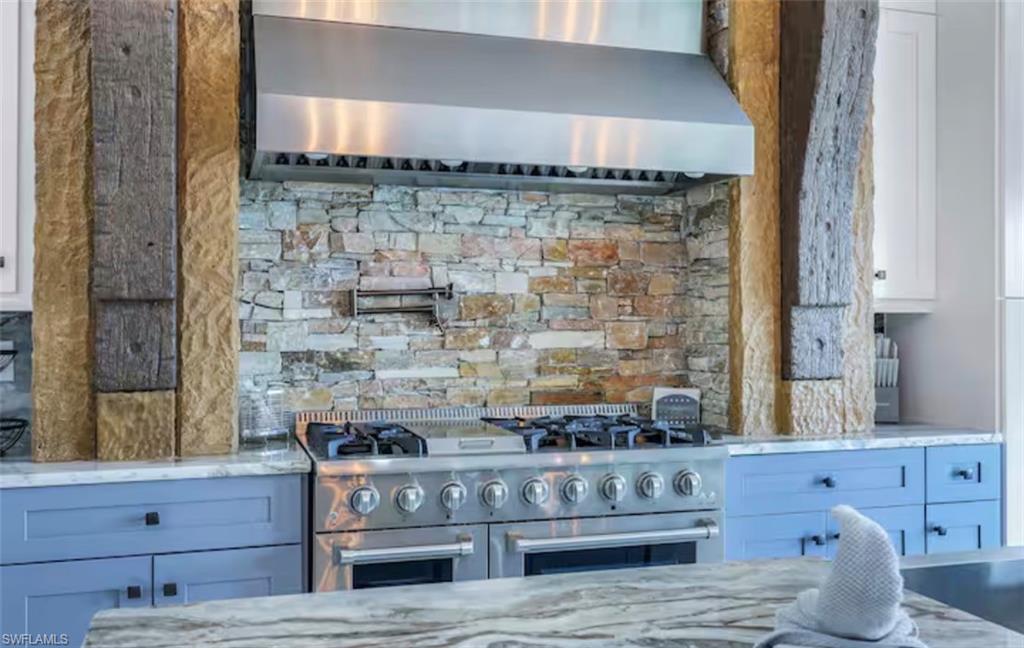 Kitchen with light stone countertops, double oven range, and white cabinets