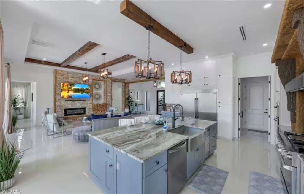 Kitchen with open floor plan, light stone countertops, premium appliances, a stone fireplace, and two tone color scheme