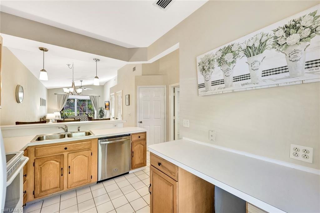 Well-lit kitchen featuring light wood-finish cabinetry, white countertops, a stainless steel dishwasher, and a double basin sink