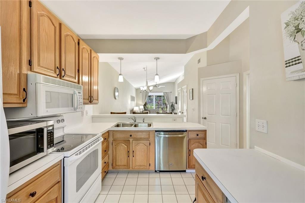 Kitchen featuring wood cabinetry, white countertops, stainless steel dishwasher, white tile flooring, and integrated microwave