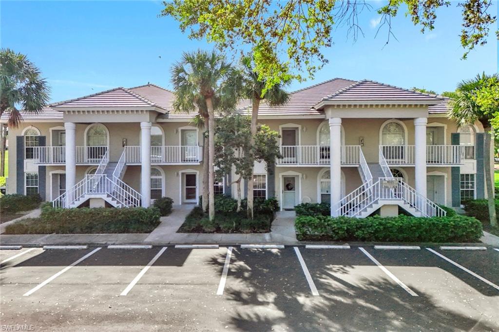 Two-story building featuring a tile roof, light-toned exterior, prominent white columns, multiple balconies with white railings, and arched windows