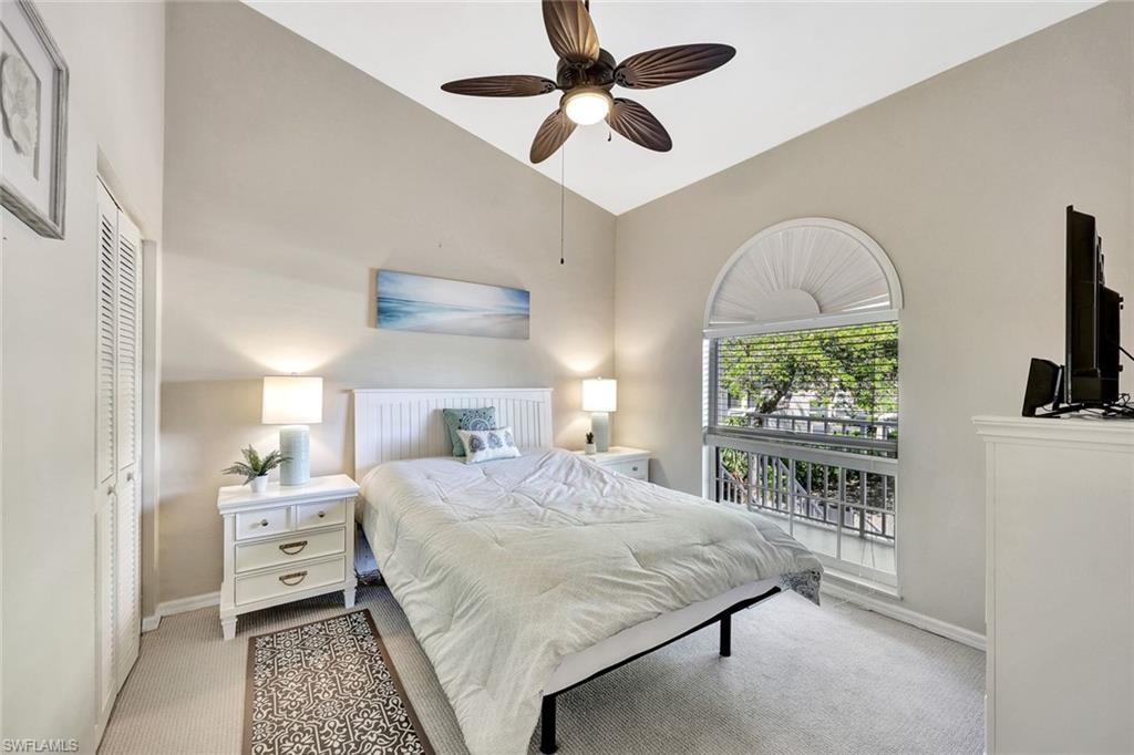 Vaulted ceiling bedroom featuring a large arched window, louvered bi-fold closet doors, and light-colored carpeting