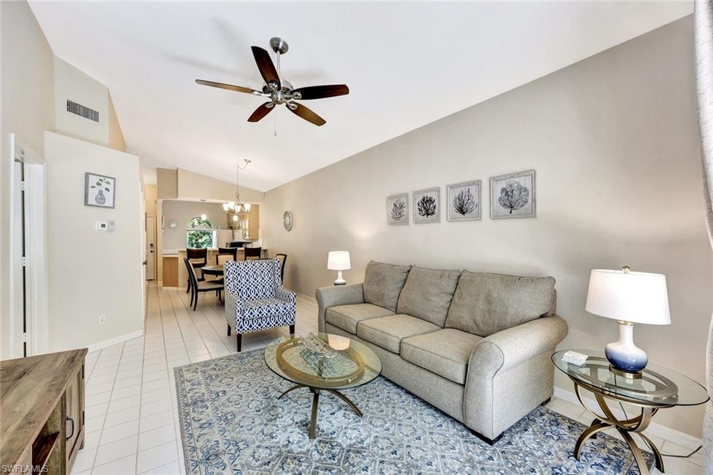 Vaulted ceilings accentuate the living space, featuring white tile flooring and a ceiling fan