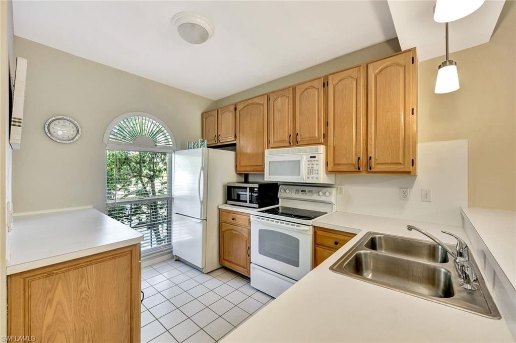 Kitchen featuring white countertops, light wood-finish cabinetry, a double basin stainless steel sink, and a large arched window with blinds