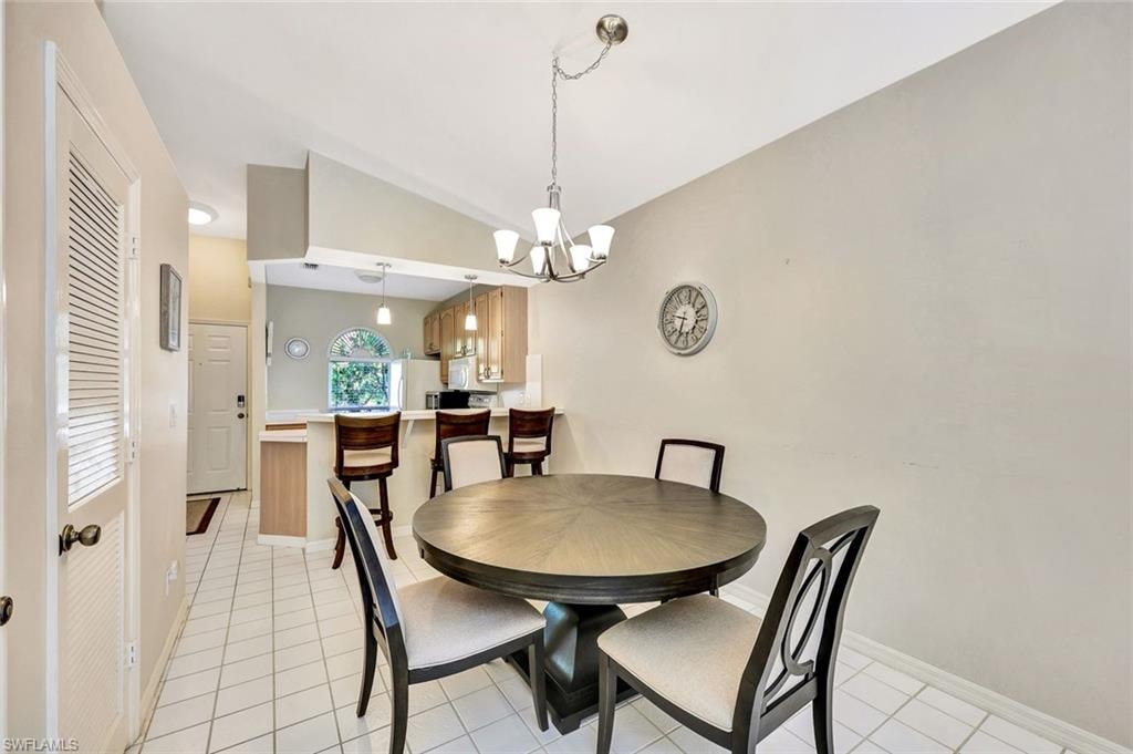 Vaulted ceiling dining area featuring tile flooring and a chandelier, with a kitchen pass-through and breakfast bar in the background