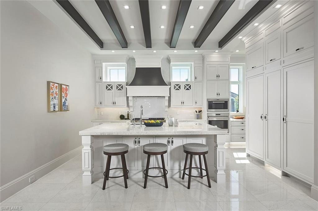 Kitchen featuring white cabinetry, a breakfast bararea, light stone counters, decorative backsplash,and beamed ceiling