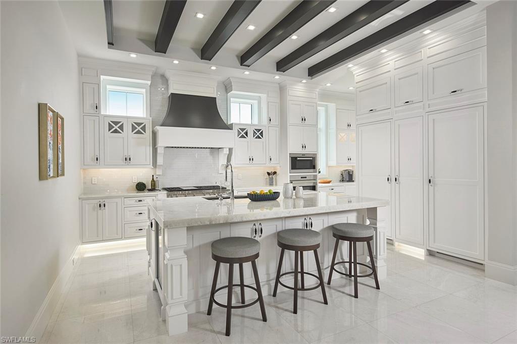 Kitchen featuring white cabinetry, a breakfast bararea, light stone counters, decorative backsplash,and beamed ceiling