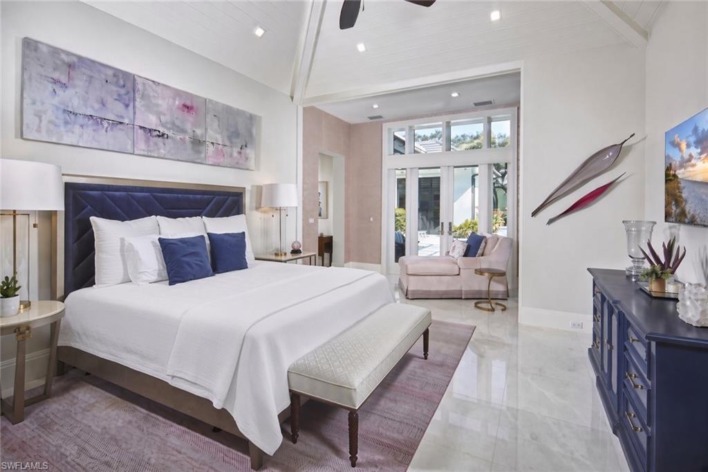 Luxurious primary bedroom featuring a navy upholstered bed with white bedding, polished stone flooring throughout, recessed ceiling lighting, and an ensuite with dual vanities visible through the open doorway