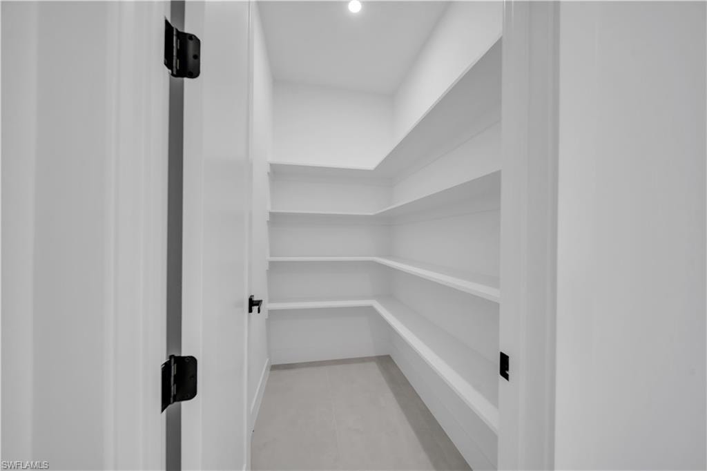Spacious pantry with multiple levels of built-in shelving, light-toned flooring, and bright overhead lighting