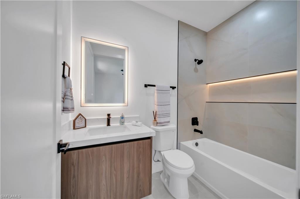 Contemporary bathroom featuring a wood-finish vanity with a white countertop and rectangular sink, an illuminated mirror, and a tiled shower/tub combination with an integrated illuminated shelf