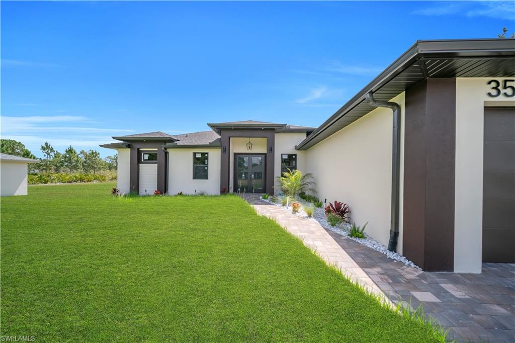 Modern exterior featuring a prominent entry, paver walkway, contemporary landscaping, well-maintained lawn, and a dark garage door