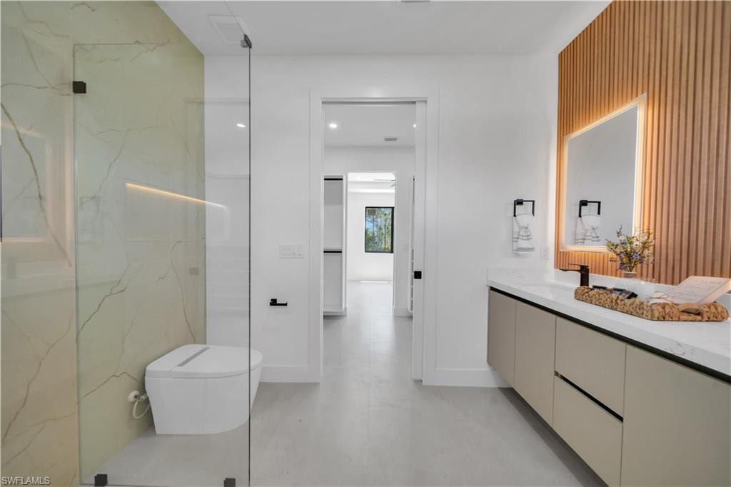 Contemporary bathroom featuring a floating vanity with a white countertop, a backlit mirror, a wood-slat accent wall, and a glass-enclosed shower with a wall-mounted toilet and marble-look wall tiling