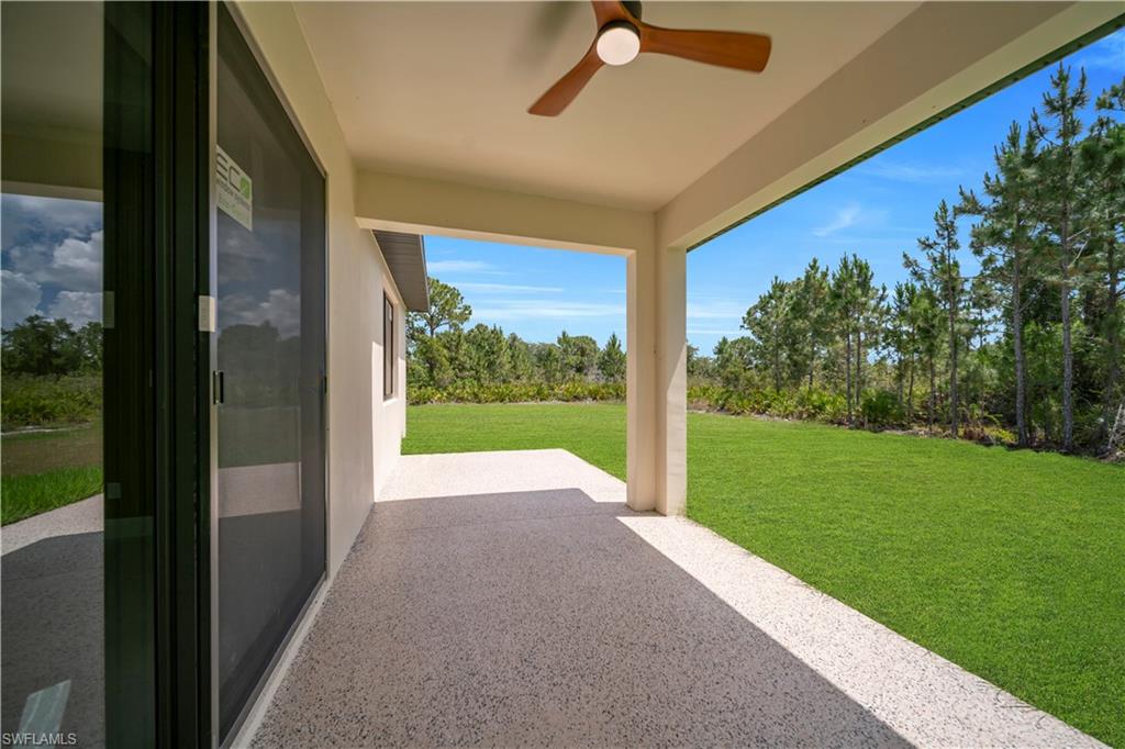 Covered patio with a wood-finish ceiling fan, full-height sliding glass door, and a textured concrete surface opening to a spacious lawn