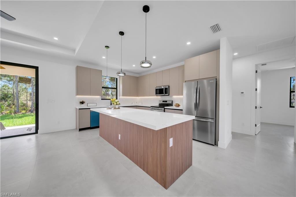 Modern kitchen featuring a large central island with a solid surface countertop, stainless steel appliances, contemporary cabinetry, under-cabinet lighting, and recessed ceiling lights