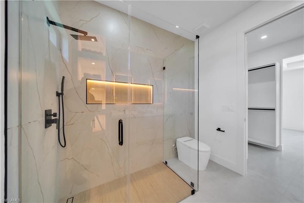 Glass-enclosed shower with a rainfall showerhead, handheld sprayer, and built-in illuminated niche