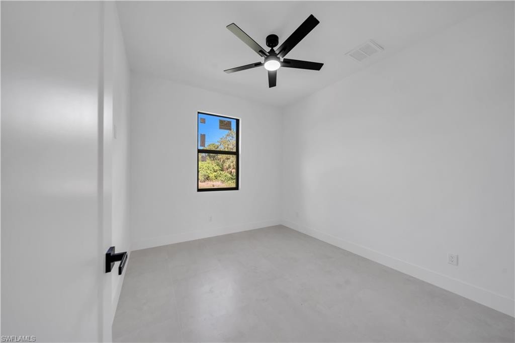 Bright room featuring a black framed window, a black ceiling fan with integrated lighting, white walls, and light-toned flooring